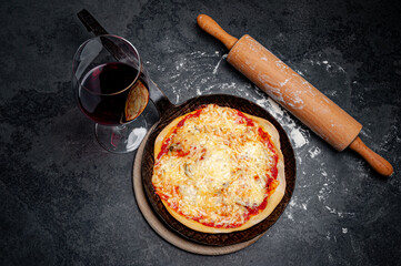 Fresh Pizza in an rustic iron Pan on a Slate Plate with a Glass of red Wine. A rolling pin lying beside and the slate is covered with flour.