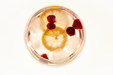 Top shot of a Gin and Tonic drink with raspberry’s and a slice of lemon. On white background with backlit.