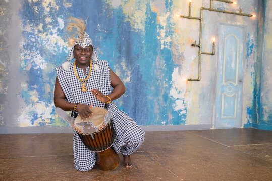 African artist in traditional clothes playing djembe drum