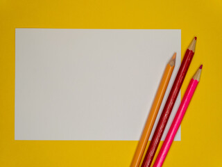 On a yellow background, a white sheet of paper and a multi colored pencils, the concept of the beginning of school classes.Copy space