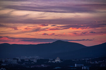 colorful view of pink clouds, mountains and buildings in the resort of Gelendzhik, against the background of a bright summer sunset. In the center of the frame is the new Orthodox Church