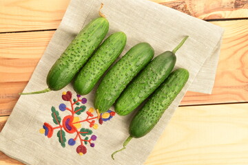 Fresh green cucumbers with a linen napkin on a wooden table.