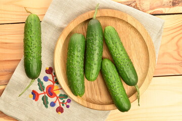Fresh green cucumbers with a linen napkin on a wooden table.