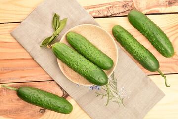 Fresh green cucumbers with a linen napkin on a wooden table.