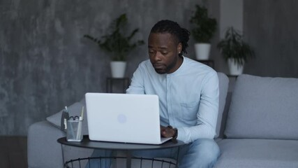 Online education, distance training, business meeting, webinar conference. Male African American freelancer working at home sitting on sofa using laptop