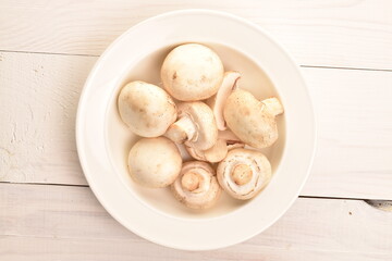 Freshly cut mushrooms on a plate, close-up, on a white wooden table.