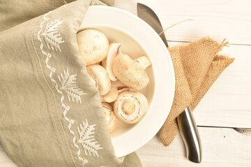 Freshly cut mushrooms on a plate with a napkin, close-up, on a white wooden table.