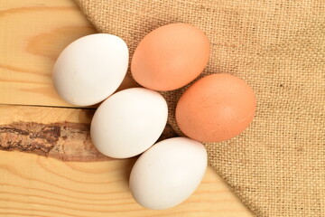 Several chicken eggs with a jute napkin, in a basket, close-up, on a wooden table.