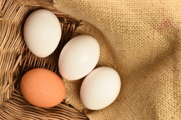 Several chicken eggs with a jute napkin, in a basket, close-up, on a wooden table.