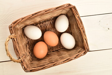 Several chicken eggs in a wicker basket, on a white wooden table.