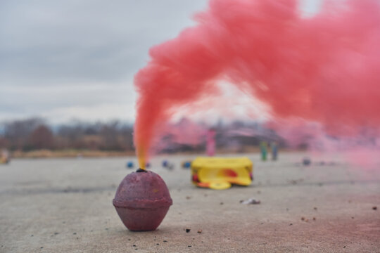 Smoke bomb emitting a pink fog with spent and used fireworks defocused in the background