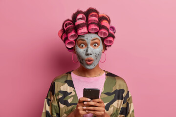 Beautiful lady has stupefied face expression, cares about face skin, applies beauty mask, wears...