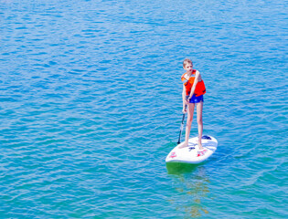 a young rider on a board for Sap surfing rakes a wave with a paddle, the concept of an active...