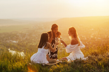 Young people having summer picnic and eating and drinking white wine together sitting on mountain top. Happy friends on mountain top having a picnic on a summer day. Copy space.
