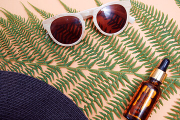Leaves of a tropical tree on a nude background. Sunglasses and hat with skin oil. The concept of rest and travel in the summer.