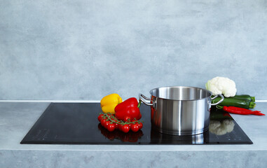 Metal pot with vegetables  on induction cooker. Modern kitchen or healthy food concept.
