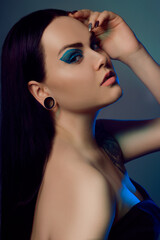  girl with tunnels in her ears in a beautiful blue light. Woman with blue make-up, fashionable blue arrows over the eyelid. Insightful brown eyes. Model with beautiful hair and professional makeup.