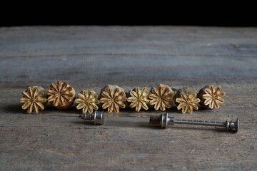 Dried opium poppy capsules and glass syringe on a wooden table against a black background