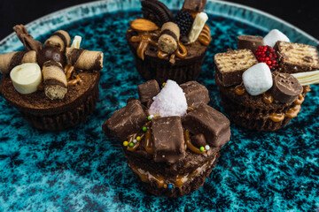 muffins stuffed with delicacy and decorated with chocolates and different sweets on blue plate with black background