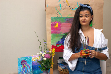 Girl holding dirty painting brushes in hands with picture on background. The artist finished the...