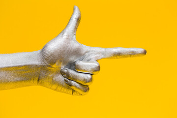 Elegant female hand with a silver paint on it shows gesture bang bang isolated on a yellow background. Free space for text