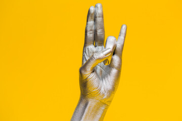 Elegant female hand with a silver paint on it isolated on a yellow background. Free space for text