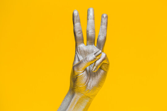 Elegant female hand with a silver paint on it shows three  fingers, isolated on a yellow background. Free space for text