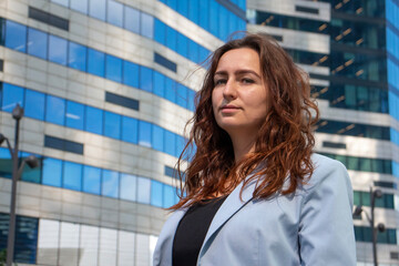 Portrait of Caucasian business woman looking at camera and wearing blue suit. Blurred office building in the background. Copy space for your text. Women in business theme.