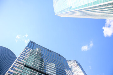 Plakat Low angle view of large skyscrapers covered with glass. Blue sky with some white clouds in the background. Modern office buildings theme.