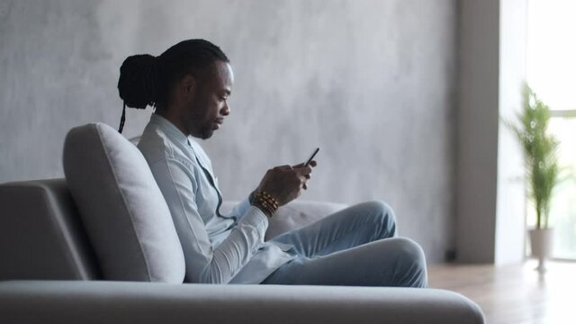 Online education, distance training, business meeting, webinar conference. African American man uses a smartphone while sitting on a sofa