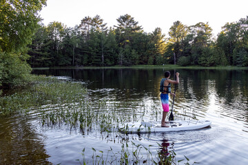 Fototapeta na wymiar teenage boy paddle boarding in reeds on lake