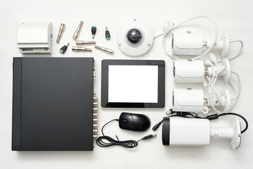Digital tablet with blank screen, video recorder and various security cameras on the white flat lay...