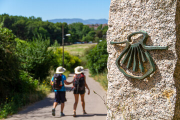 Pilgrims on the route of the Camino de Santiago (Way of Saint James) passing next to the scallop shell that marks the way