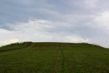 Obraz premium The green grass hill landscape with the gray clouds in sky.