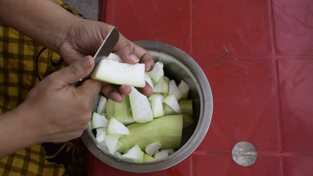 Cutting of Vegetable by a small knife into small pieces. Indian house wife chopping bottle gourd into small pieces and putting them in the steel bowl