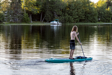 Fototapeta na wymiar Teenage boy paddle boarding on lake