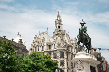 Fototapeta na wymiar Liberty square in the historic center of Porto with statue of King Pedro IV on top of a horse in front in the foreground with a majestic building during a very sunny day in Portugal