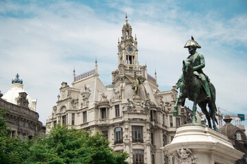 Fototapeta na wymiar Liberty square in the historic center of Porto with statue of King Pedro IV on top of a horse in front in the foreground with a majestic building during a very sunny day in Portugal