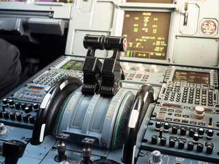 Airbus A320 thrust levers on the center instrument panel. Switches and dials visible in the background. 