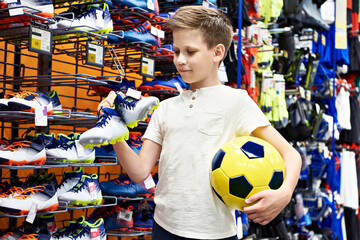 Boy with ball and boots in football sport store