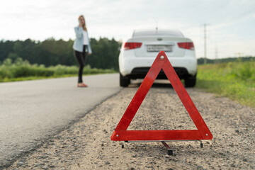 Close up on triangle warning sign with woman calling for assistance after breaking down with her...