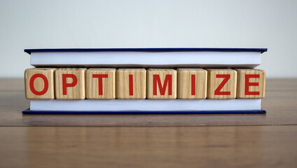 Concept word 'optimize' on wooden cubes between pages of a book on a beautiful wooden table. White background. Business concept.