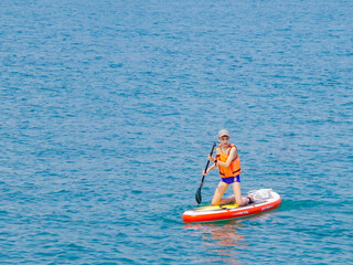 a young rider on a board for Sap surfing rakes a wave with a paddle, the concept of an active...