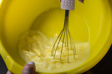 Chef with a whisk whips the pancake dough in a yellow plastic bowl	
