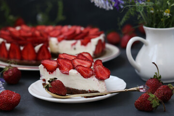 Chopped homemade strawberry cheesecake, decorated with fresh strawberries, on a plate on a dark background, close-up, horizontal format