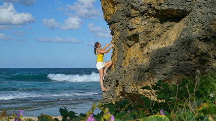 Traveler stops at the beach to climb a boulder overlooking the blue ocean.