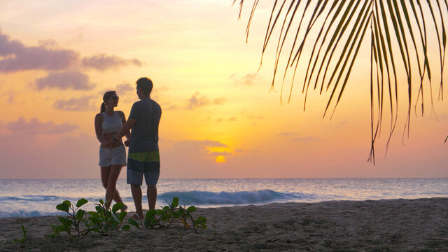 LOW ANGLE: Carefree young tourist couple dances on white sand beach at sunset
