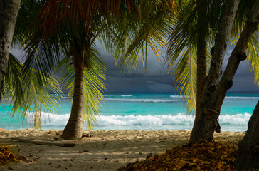 Fototapeta na wymiar CLOSE UP: Dark stormy skies span above the turquoise ocean washing sandy beach