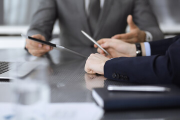 Unknown businessman using tablet computer and working together with his colleague while sits at the glass desk in modern office. Teamwork and partnership concept
