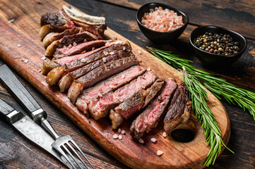 Grilled cowboy or rib eye beef steak with herbs and spices.  Wooden dark background. Top view.